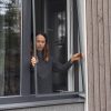 En kvinde står ved et åbent vindue og monterer et Myggenet til vindue - med ramme på ydersiden af bygningen.