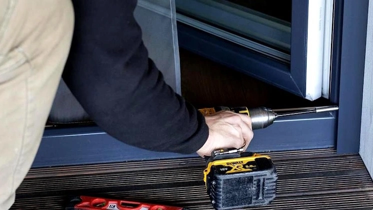 Person using a cordless drill to install a sliding door frame at home, with tools and a Roll-Up Insect Screen from Insectnets.com nearby.